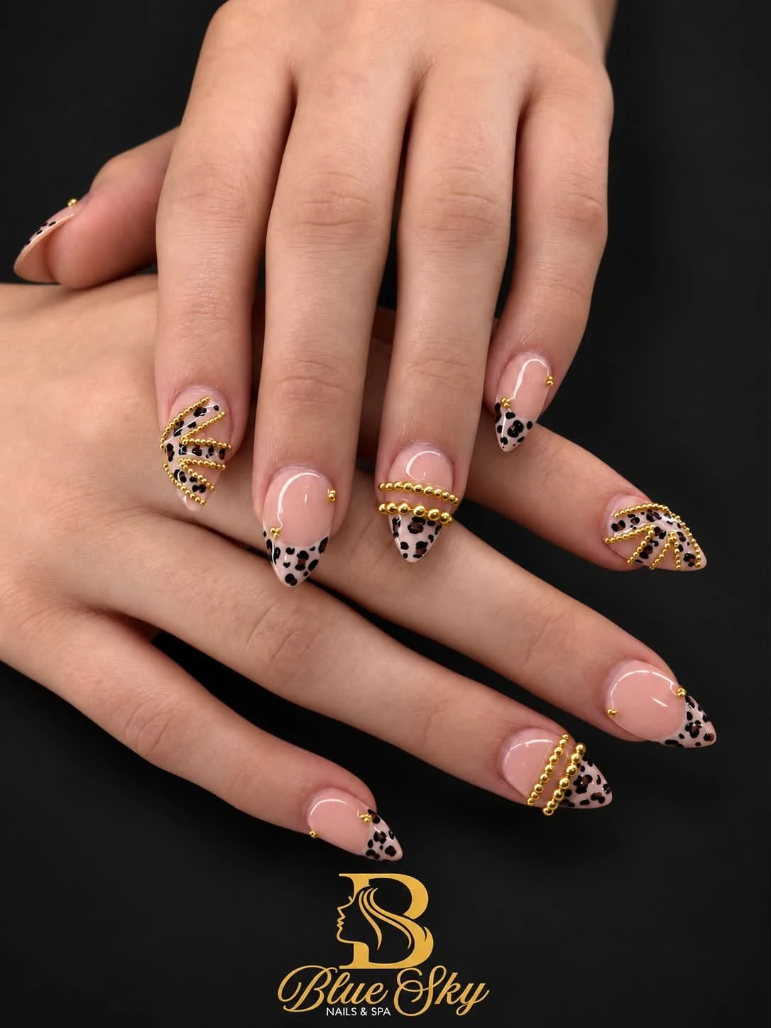 Nude almond nails with leopard-print French tips and small gold accents