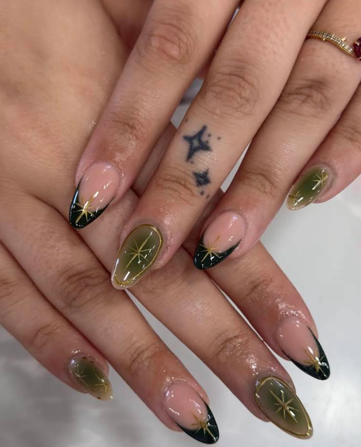 Olive green and dark French-tip nails with fine gold starbursts